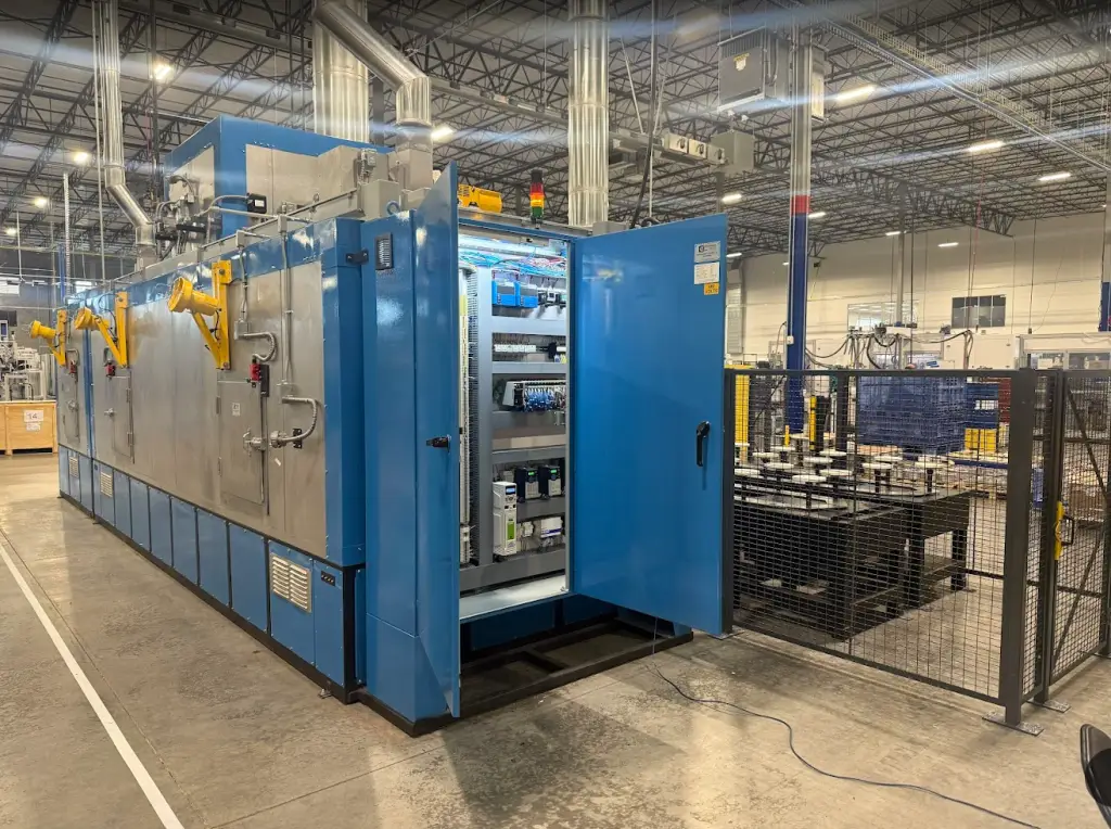 Industrial finishing oven with open electrical control panel showing PLCs, drives, and automation components.