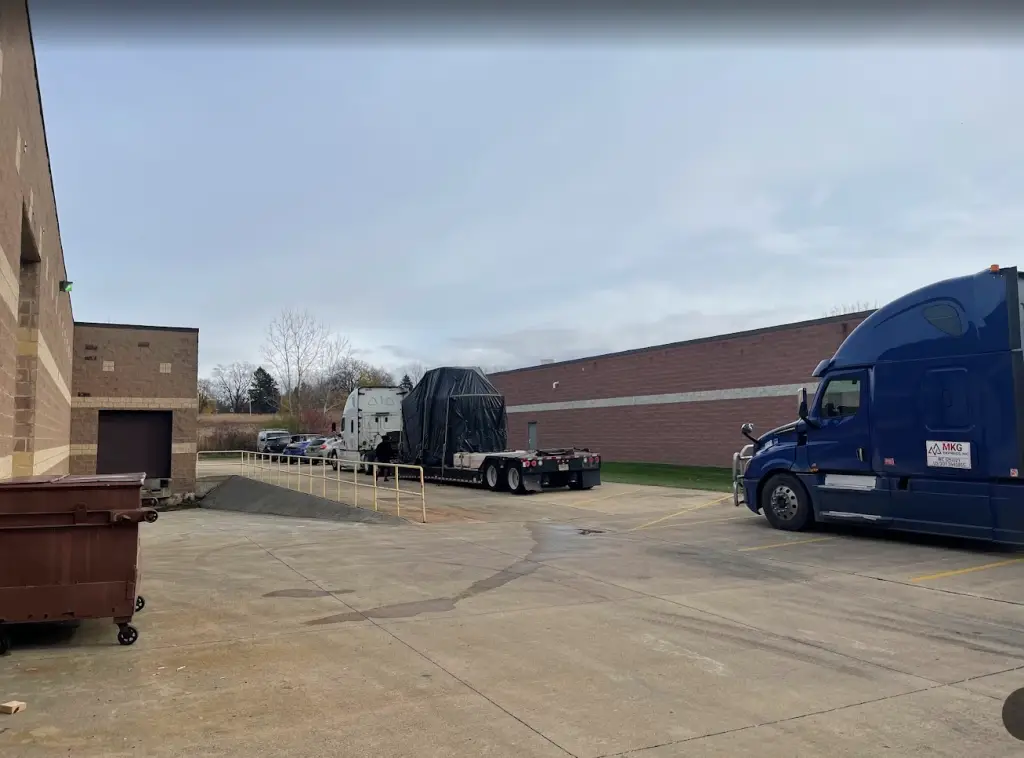 Flatbed truck being loaded with an industrial finishing system at Precision Conveyor's shipping dock.