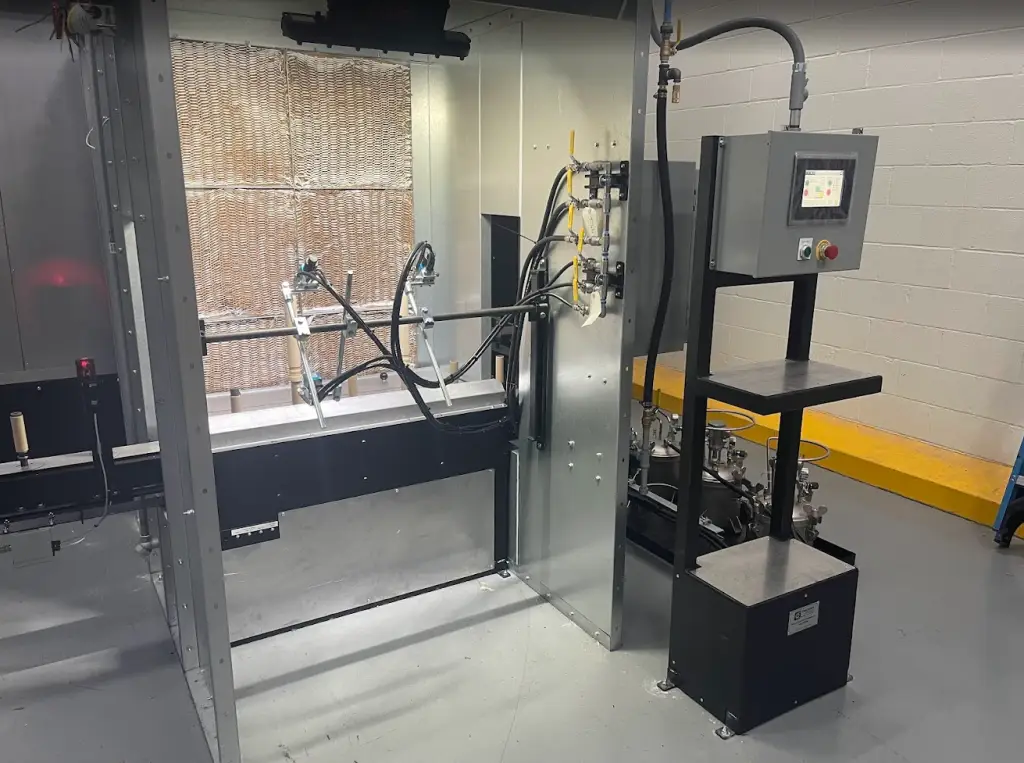 Custom-built spray booth with fluid delivery system, air cap controls, and exhaust filtration for liquid paint application.