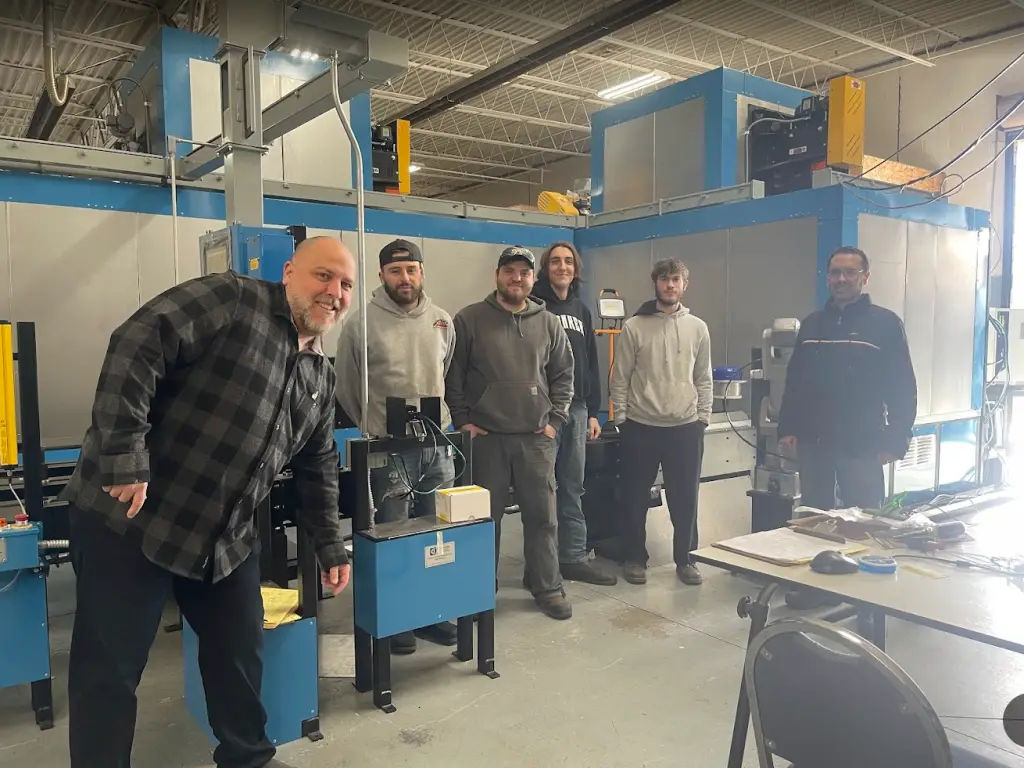 Group of employees and engineers standing in front of an automated finishing system during final assembly.