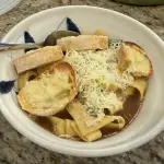 Bowl of French onion beef and noodles topped with cheesy Gruyère bread – slow braised chuck roast with caramelized onions and pasta in rich broth