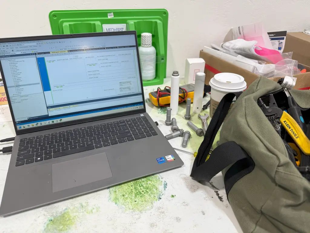 Job site engineering setup in Arizona with laptop, tools, coffee, and aerospace fastener coating fixtures during system startup