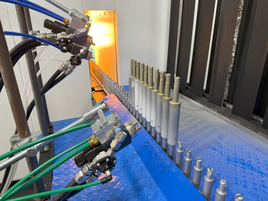Close-up of spray gun with infrared preheat oven in the background during aerospace fastener coating system startup in Arizona