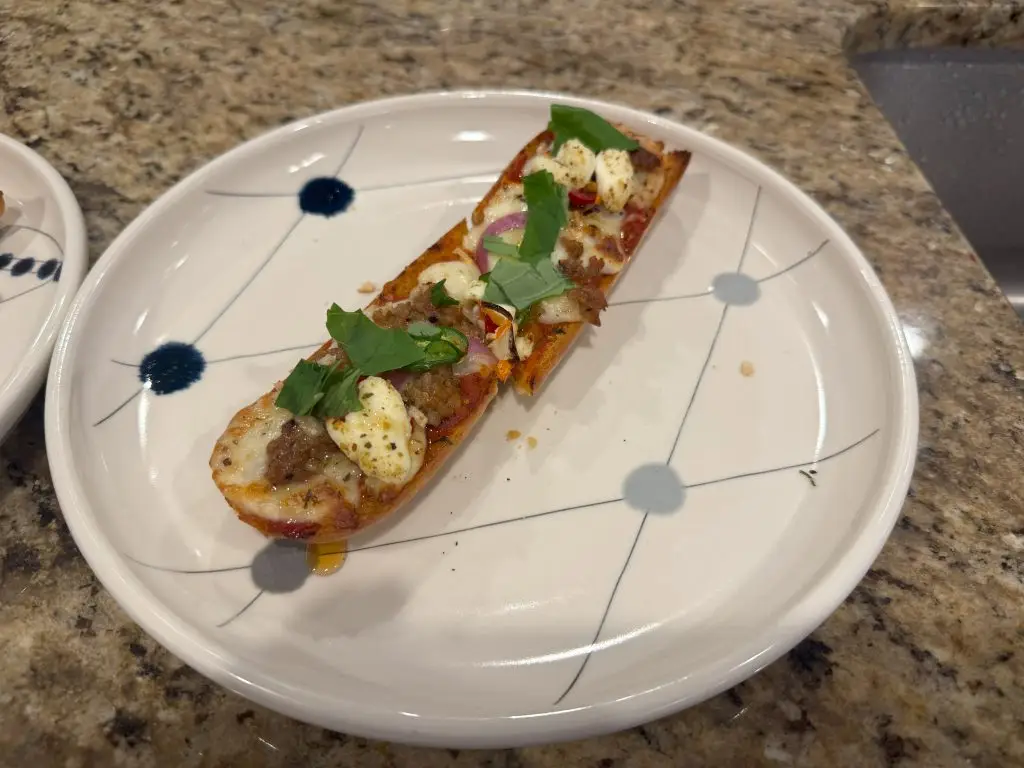 A crispy French bread pizza topped with spicy Italian sausage, dollops of ricotta, melted mozzarella, and a drizzle of golden hot honey, finished with fresh basil leaves.