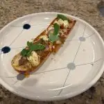 A crispy French bread pizza topped with spicy Italian sausage, dollops of ricotta, melted mozzarella, and a drizzle of golden hot honey, finished with fresh basil leaves.