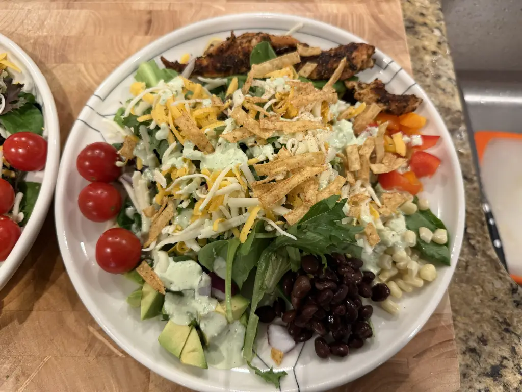 Grilled Cajun chicken slices over fresh greens with colorful peppers, avocado, and creamy dressing drizzle.