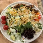 Grilled Cajun chicken slices over fresh greens with colorful peppers, avocado, and creamy dressing drizzle.