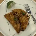 Close-up photo of crispy birria tacos filled with shredded beef and melted cheese, seared to a golden brown and topped with fresh cilantro and diced onion.