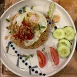 Chicken Nasi Goreng with fried egg, dark caramelized rice, and house-made sambal served with cucumber and tomato
