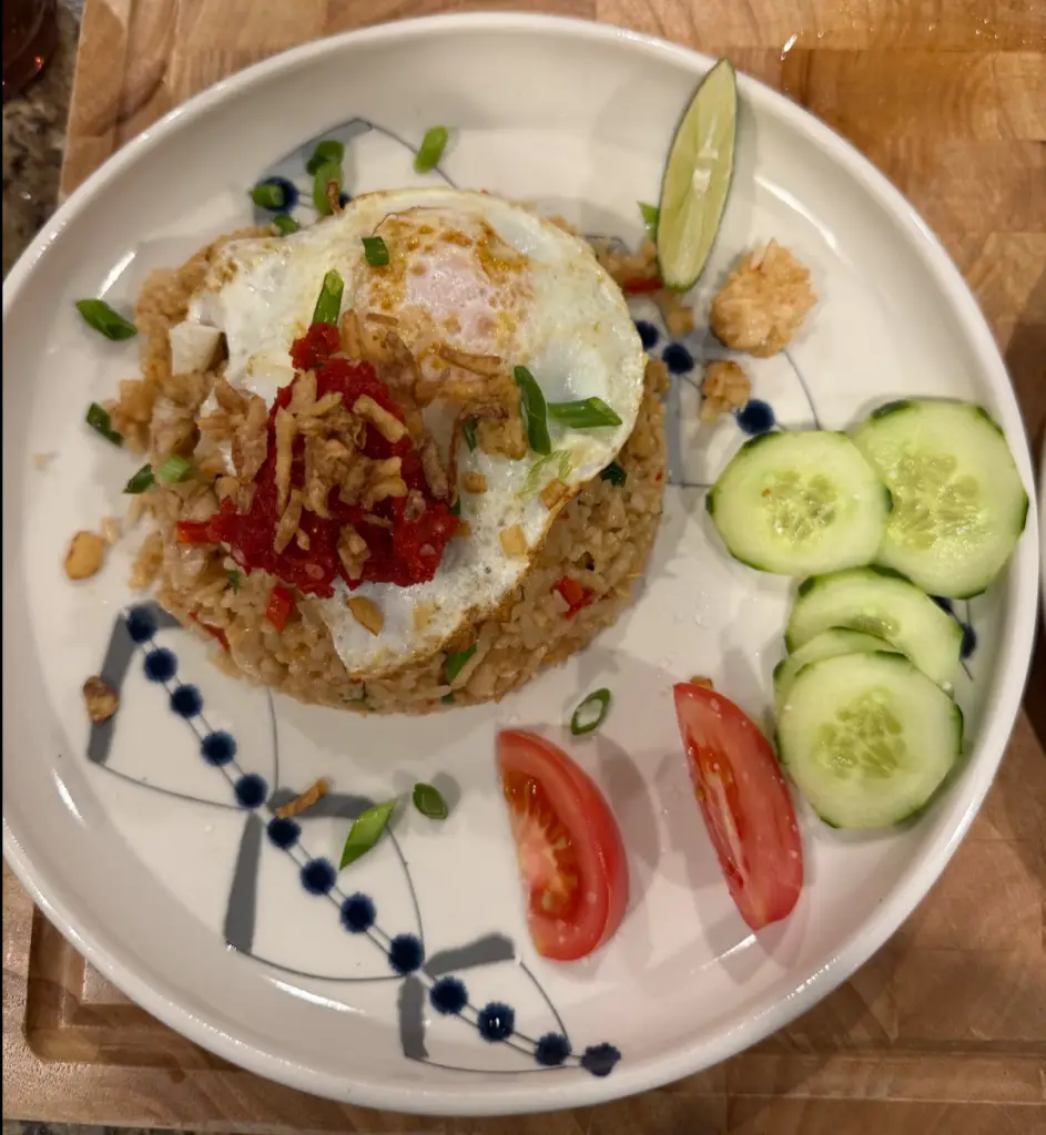 Chicken Nasi Goreng with fried egg, dark caramelized rice, and house-made sambal served with cucumber and tomato