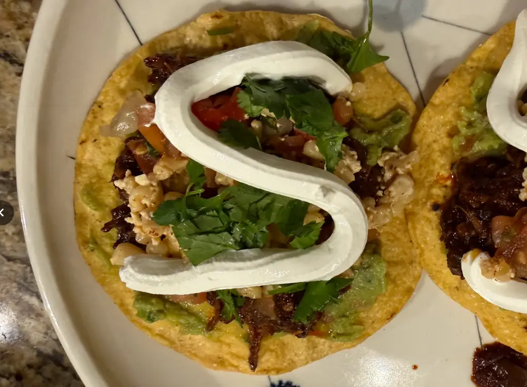 Chipotle chile braised beef tostadas topped with street corn, avocado, cotija cheese, and sour cream on crispy corn tortillas