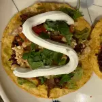 Chipotle chile braised beef tostadas topped with street corn, avocado, cotija cheese, and sour cream on crispy corn tortillas
