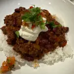 Spicy ground beef chili con carne served over white rice with fresh pico de gallo and sour cream.